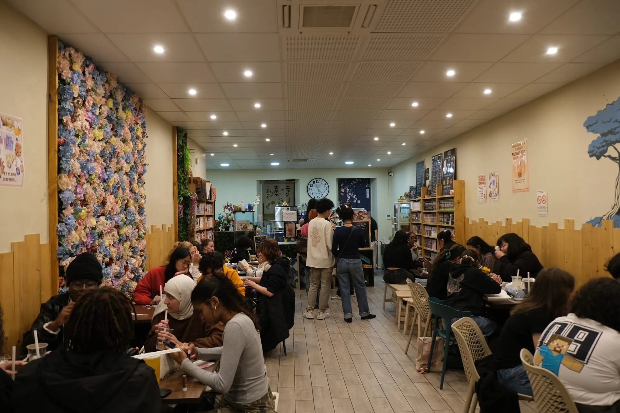 La salle de Sweet Bubble Thé remplie de clients, devant le mur de fleurs
